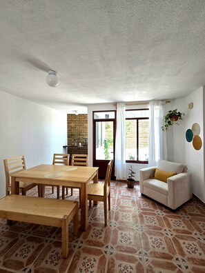 A room with a wooden dining table, chairs, a sofa, and a window with curtains. - A great location with contemporary comfort and the richness of Oaxacan culture. (Oaxaca de Juárez)