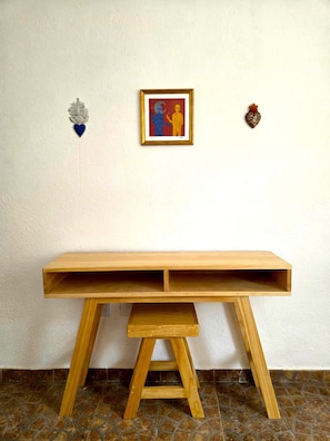 A wooden desk with a shelf, positioned against a white wall with a framed artwork and two decorative items. - A great location with contemporary comfort and the richness of Oaxacan culture. (Oaxaca de Juárez)