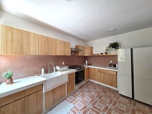 A modern kitchen with wooden cabinets, a stainless steel sink, and a white refrigerator. - A great location with contemporary comfort and the richness of Oaxacan culture. (Oaxaca de Juárez)