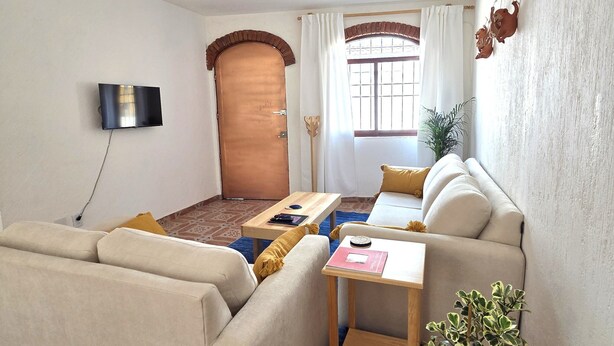 A compact living space with a sofa, a small table, a potted plant, and a television mounted on the wall. - A great location with contemporary comfort and the richness of Oaxacan culture. (Oaxaca de Juárez)