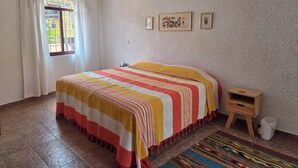 A bedroom with a bed, a small wooden nightstand, a colorful rug, and a window with curtains. - A great location with contemporary comfort and the richness of Oaxacan culture. (Oaxaca de Juárez)