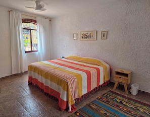 A bedroom with a bed, a small wooden nightstand, a colorful rug, and a window with curtains. - A great location with contemporary comfort and the richness of Oaxacan culture. (Oaxaca de Juárez)