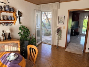 A room with a dining table set, a chair, a plant, a clock, and a door leading to an outdoor area. - Casa Ruf - Near Europa-Park (Hohberg)