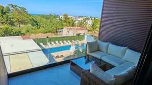 A modern balcony with a glass-top table, wicker sofa, and a view of a swimming pool and greenery. - Surf One (Sosúa)