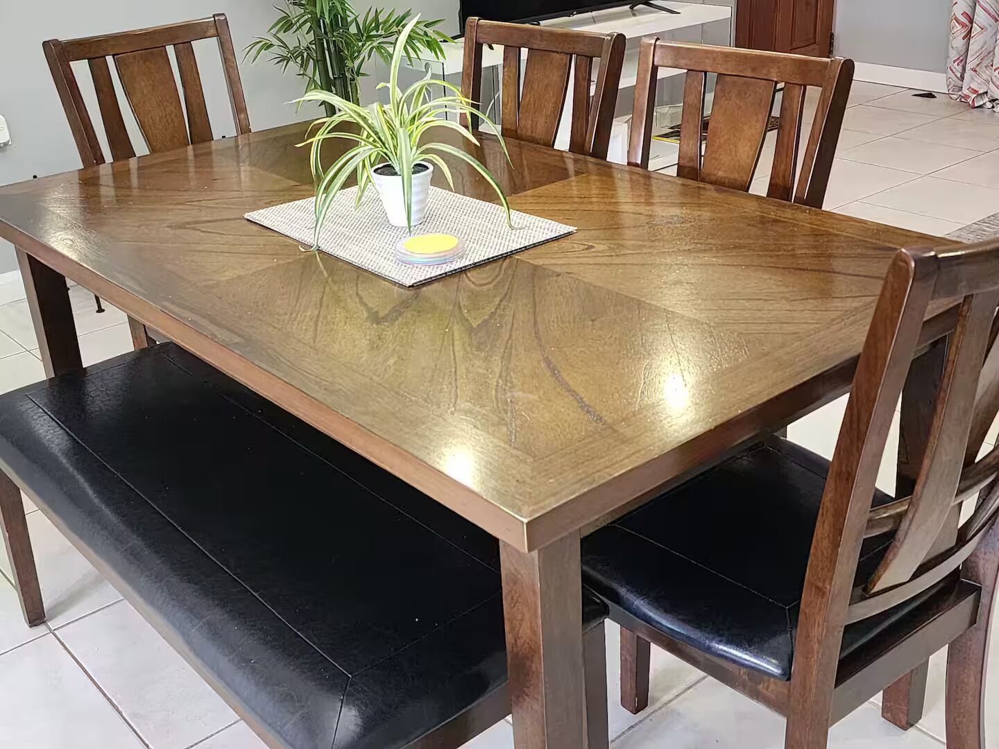 A dining table with six wooden chairs, a potted plant, and a placemat.