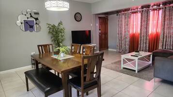 A dining area with a wooden table and chairs, a television, and a ceiling fan.