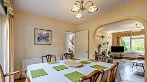 A dining area with a table set for four, chairs, a chandelier, a framed picture on the wall, and a view of the garden through an archway. - Host & Stay | Worthing Getaway (Worthing)