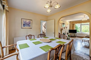A dining area with a table set for four, chairs, a chandelier, a framed picture on the wall, and a view of the garden through an archway. - Host & Stay | Worthing Getaway (Worthing)