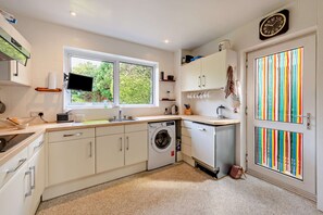A modern kitchen with a built-in washing machine, a window with a view of greenery, and a colorful striped door. - Host & Stay | Worthing Getaway (Worthing)
