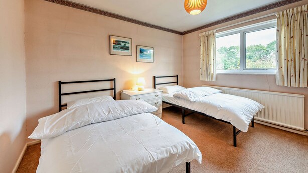 A bedroom with two beds, a nightstand with a lamp, a window with curtains, and two framed pictures on the wall. - Host & Stay | Worthing Getaway (Worthing)