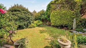 A well-maintained garden with a variety of plants and flowers, a clear lawn, and a stone structure in the foreground. - Host & Stay | Worthing Getaway (Worthing)