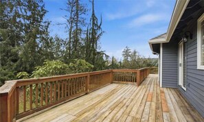 A wooden deck with a railing, surrounded by trees and a building with a gray siding.