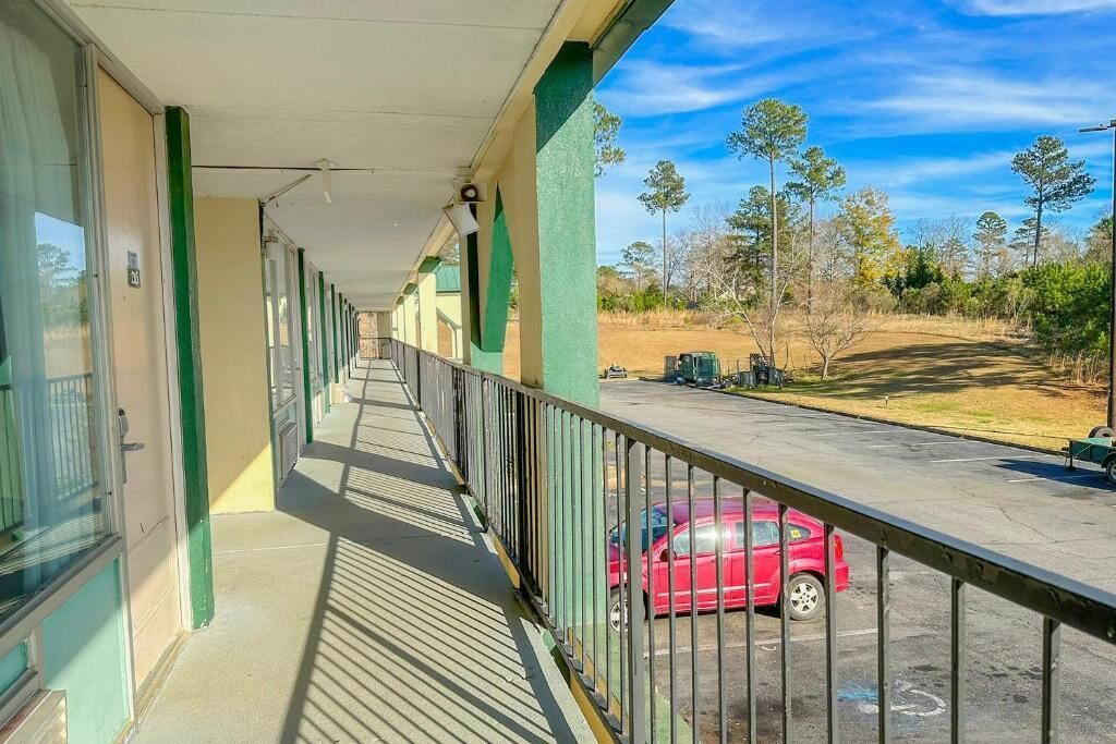 Un couloir donnant sur un balcon qui offre une vue sur un parking et des arbres.