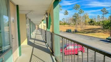 Un couloir donnant sur un balcon qui offre une vue sur un parking et des arbres.