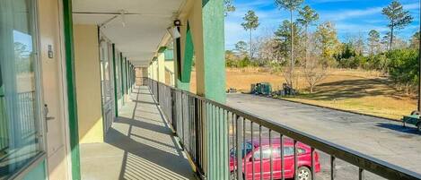 A corridor with a balcony overlooking a parking area and trees.