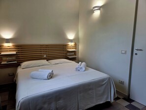 A hotel room with a bed, two bedside lamps, a door, and a towel on the bed.