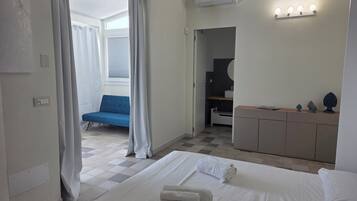Una camera d'hotel con un letto, una poltrona blu, una toeletta con uno specchio e un bagno visibile attraverso una porta aperta.