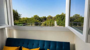 A room with a blue sofa and yellow cushions, a window with a view of trees and a railing.