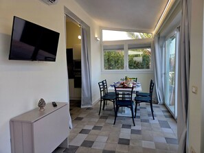 Un comedor con una mesa dispuesta para cuatro personas, un televisor montado en la pared y una cocina al fondo.