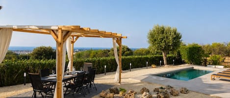 Un espacio cubierto para comer al aire libre, con piscina y vistas al mar.