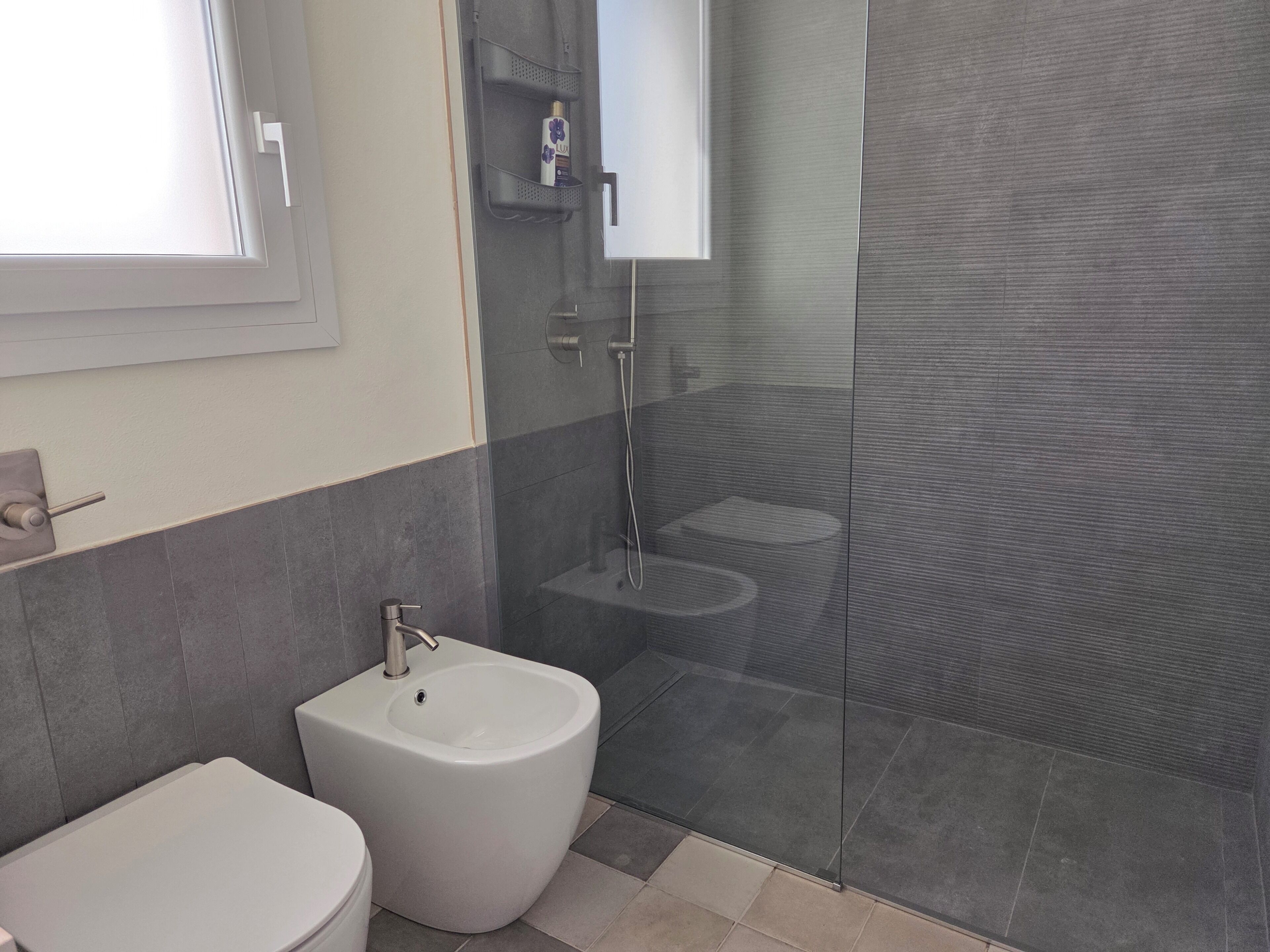 Une salle de bain comprenant des toilettes, un bidet et une douche séparée par une paroi en verre.