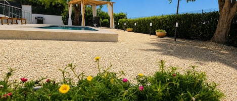 A pool area with a pergola, surrounded by gravel and potted plants.