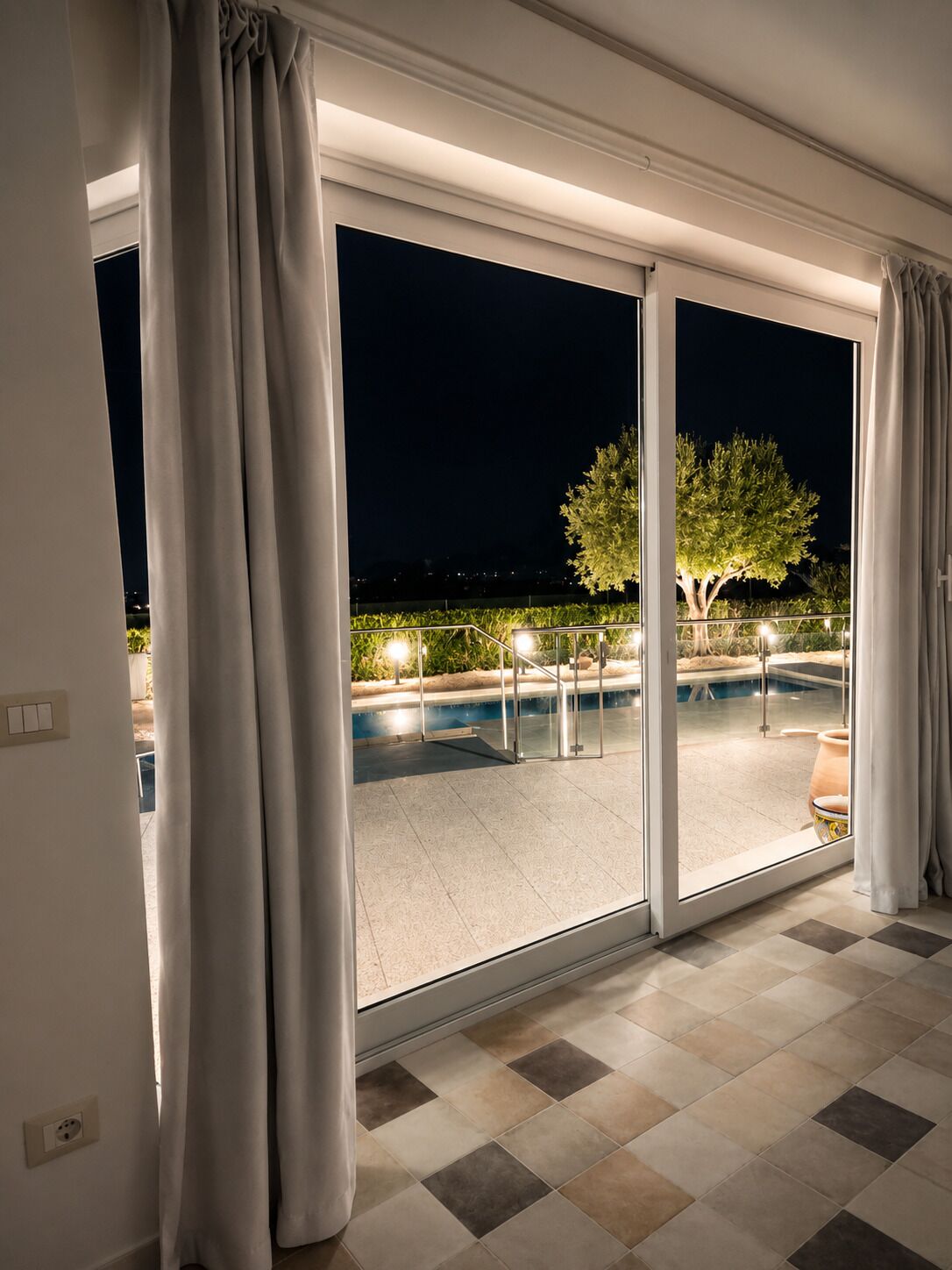 Une pièce dotée d’une grande porte-fenêtre coulissante donnant sur une piscine extérieure, le tout illuminé la nuit.