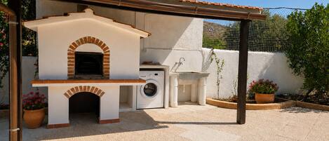An outdoor kitchen area with a brick oven, washing station, and potted plants.