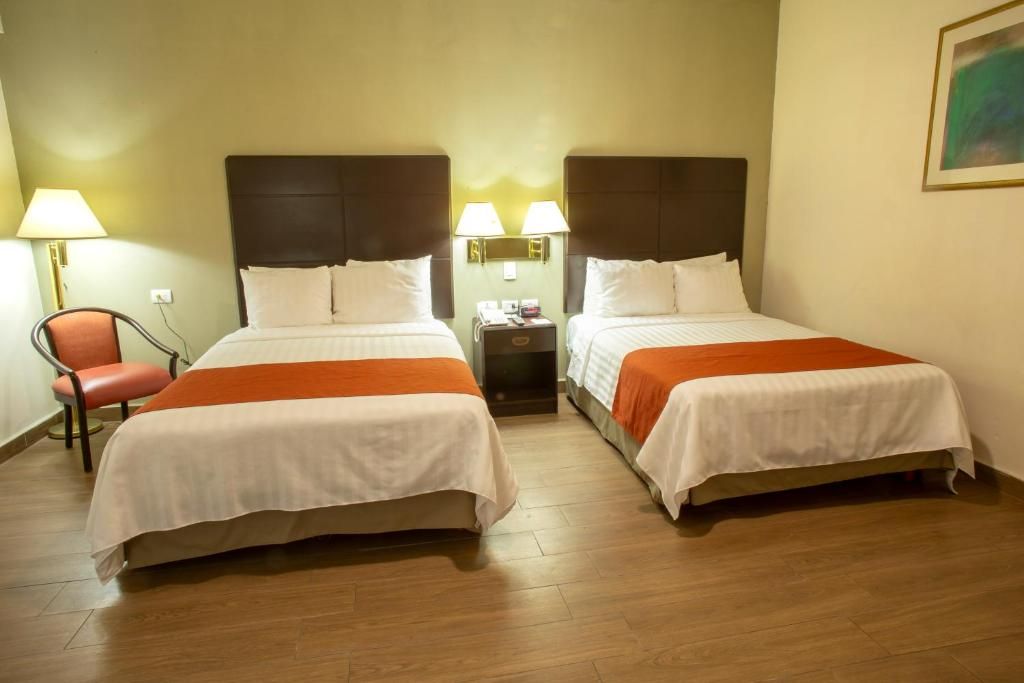 A hotel room with two beds, a nightstand, a chair, and a lamp.