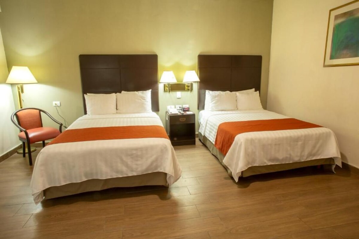 Una camera d'albergo con due letti, un comodino, una sedia e una lampada.