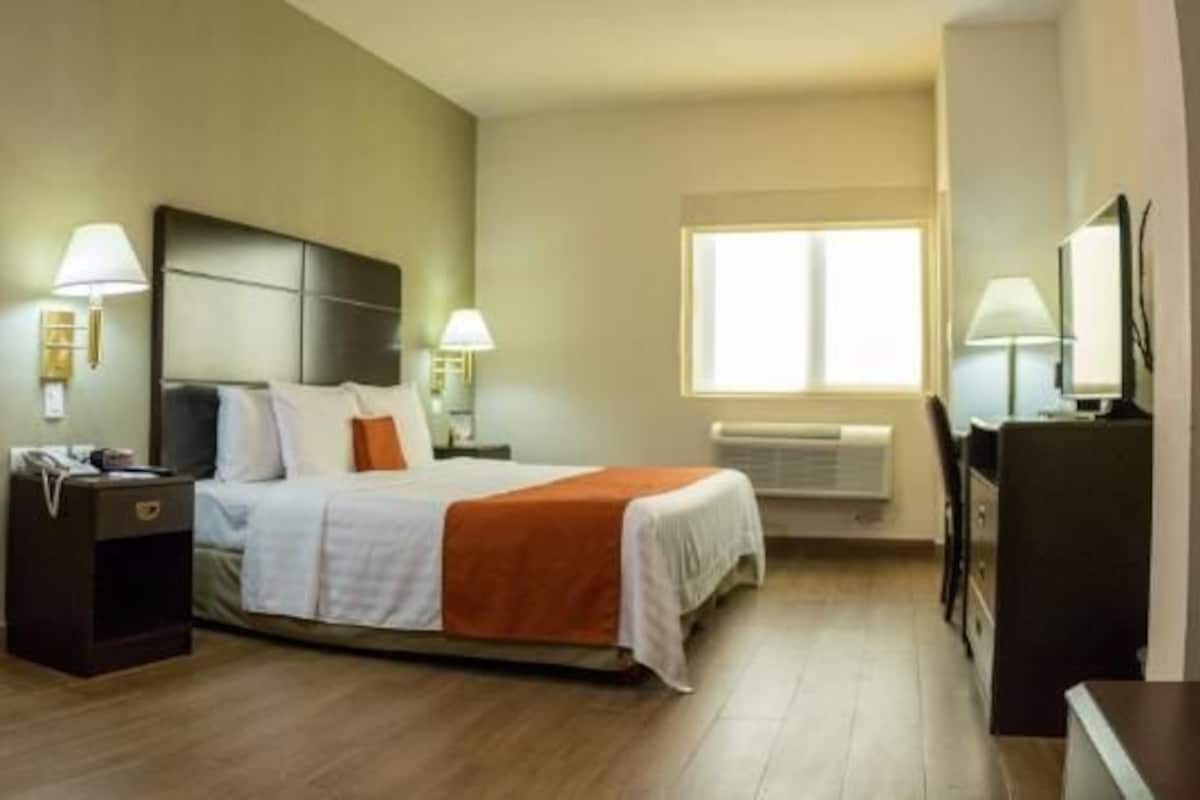 Una camera d'albergo con un letto, una scrivania, due sedie, una lampada, un comodino e una finestra.