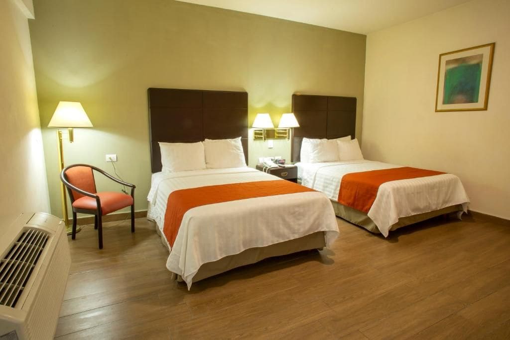 Une chambre d’hôtel avec deux lits, une chaise, une lampe et un tableau au mur.