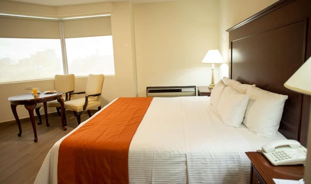 Een hotelkamer met een bed, een bureau, een stoel, een lamp en een raam.