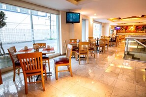 Un ristorante con sedie e tavoli di legno, una televisione a parete e vista sulla strada.