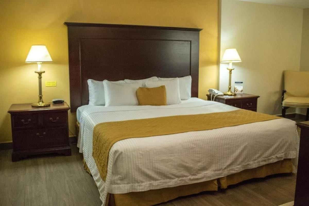 Una camera d'albergo con un letto grande, due comodini con lampade, una sedia e una testiera in legno.