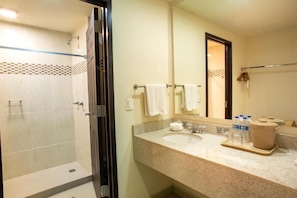 Un bagno d'albergo con doccia, lavandino, specchio e porta asciugamani.