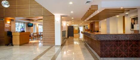 Un vestíbulo de hotel con mostrador de recepción, zona de estar y escalera.