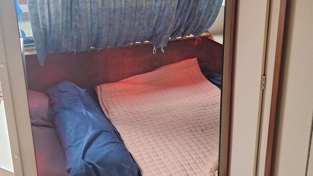 A compact sleeping area with a bed, a quilted blanket, and a curtain. - The Pink Lady Yacht - Beautiful Providence Marina (Providence)