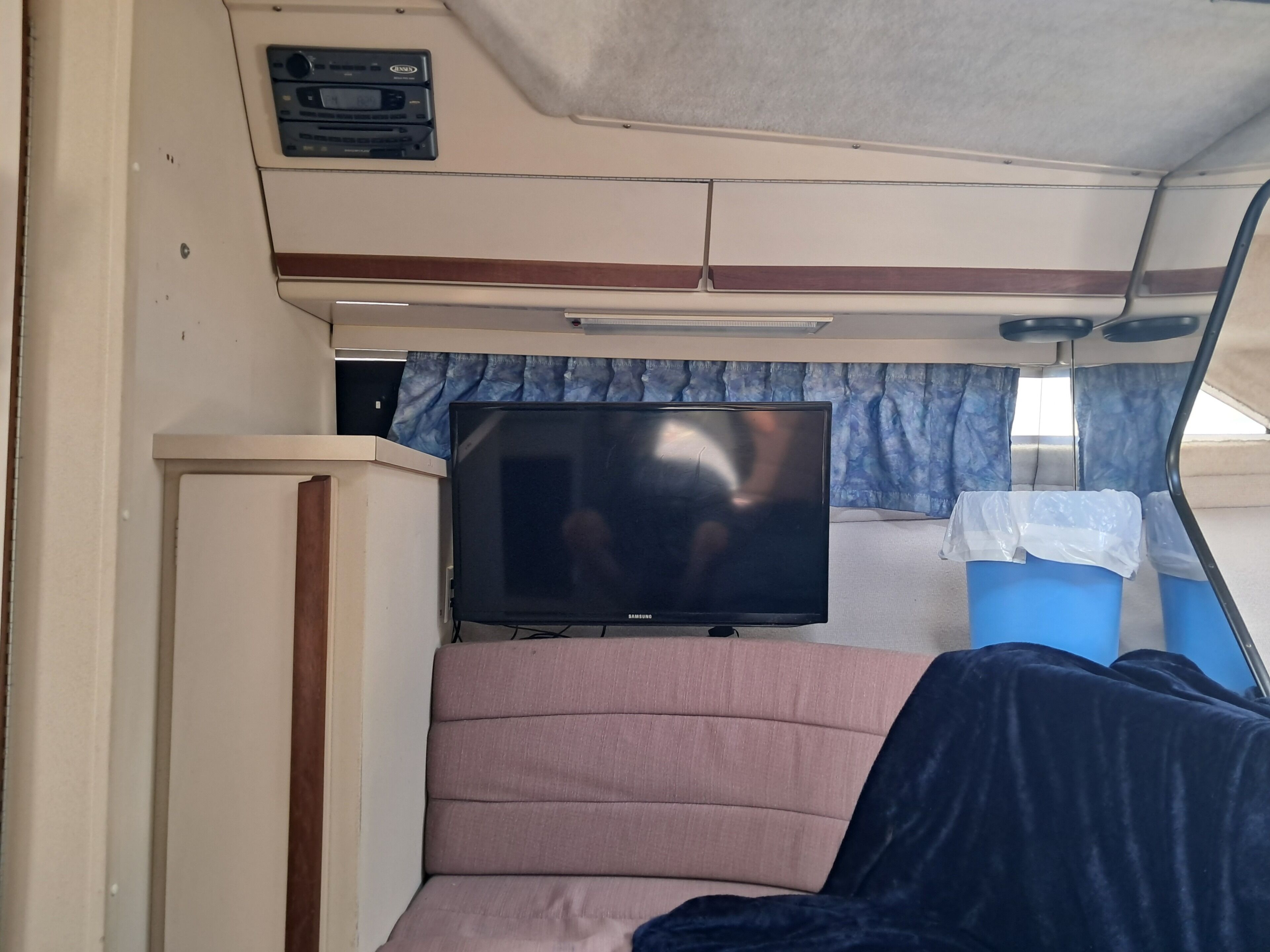 A compact living space with a television, a cushioned seating area, and storage bins.