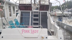 A boat named 'Pink Lady' docked at a marina with a covered seating area and a ladder leading to the upper deck. - The Pink Lady Yacht - Beautiful Providence Marina (Providence)