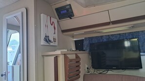 A room with a bed, a television mounted on the wall, a small table, and a door leading to another room. - The Pink Lady Yacht - Beautiful Providence Marina (Providence)