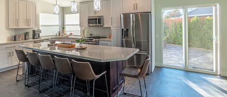 A modern kitchen with a large island, bar stools, stainless steel appliances, and a view to the outside.