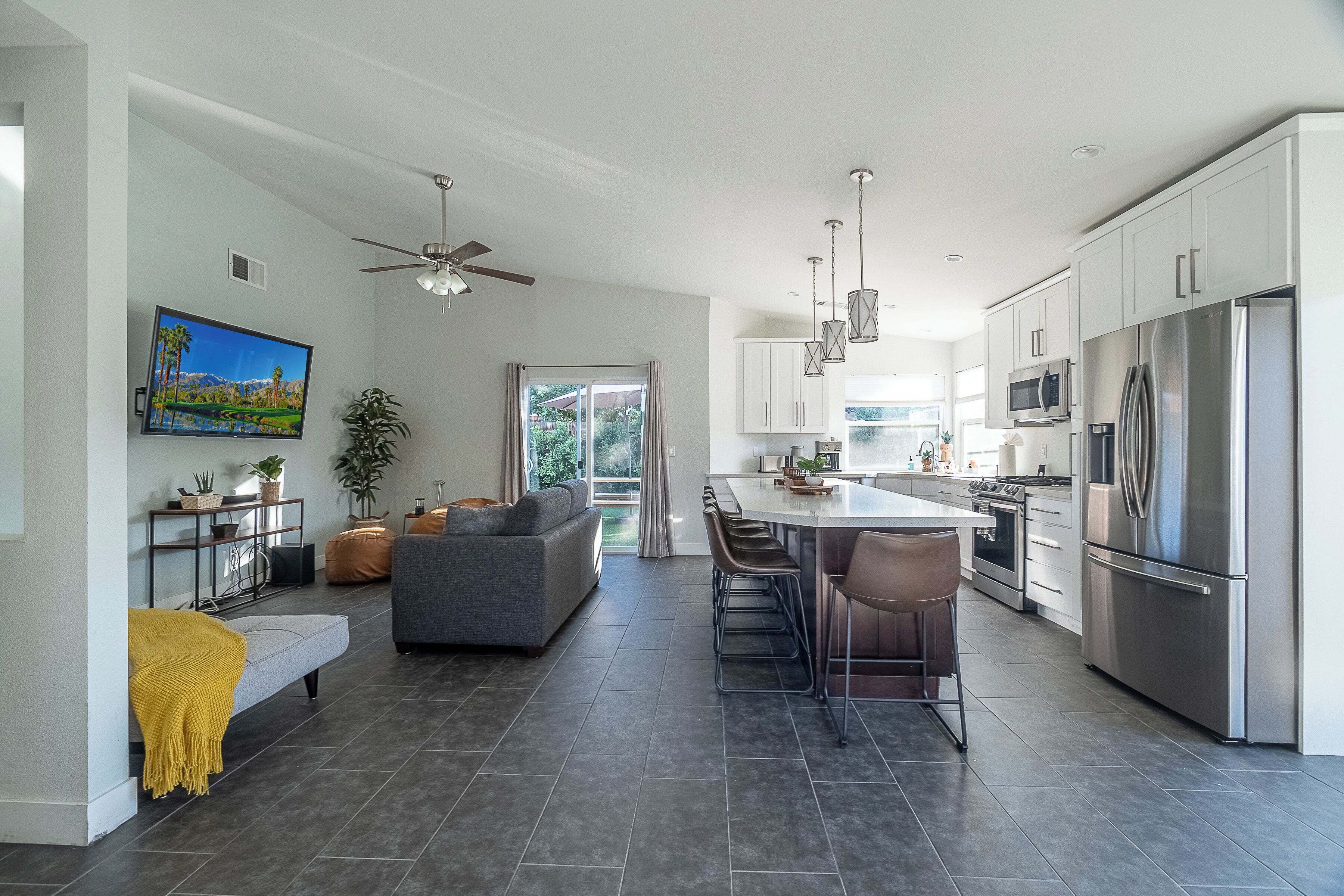 A modern kitchen with stainless steel appliances, a dining area with bar stools, and a living room with a sofa and a television.