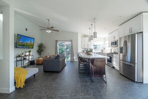 A modern kitchen with stainless steel appliances, a dining area with bar stools, and a living room with a sofa and a television. - Stylish 3-Bedroom Indio Retreat with Pool, A/C, and Modern Comforts (Las Vegas)