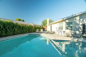 A swimming pool with a clear blue water surface, surrounded by a hedge and a building with a white exterior. - Stylish 3-Bedroom Indio Retreat with Pool, A/C, and Modern Comforts (Las Vegas)