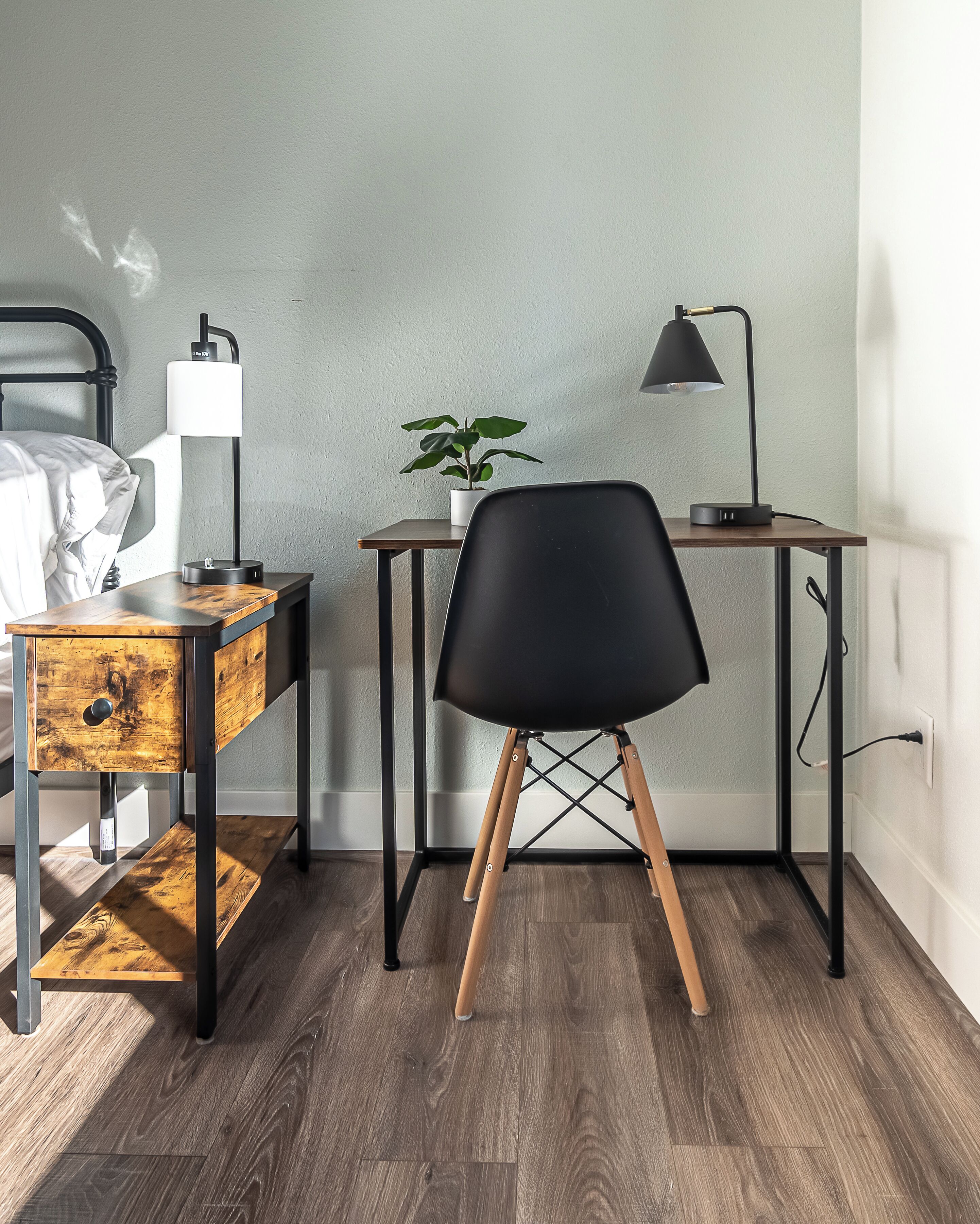 Une pièce comprenant un lit, un bureau avec une lampe, une chaise et une petite plante.