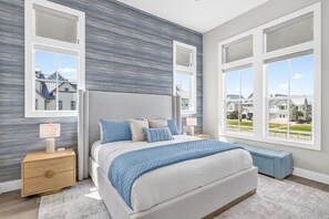 A bedroom with a bed, bedside tables, a bench, and large windows. - Vacay all Day 115 DEW (Port Aransas)