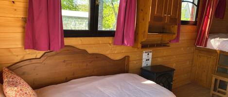 Une pièce de cabane en bois comprenant un lit, une petite table et une fenêtre avec des rideaux.