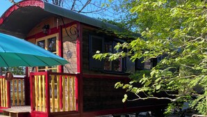 A wooden structure with a red and yellow facade, a covered seating area, and a gravel ground. - Charmante Roulotte au Cœur de la Nature (Pigny)