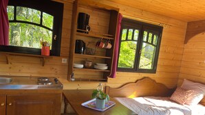 A wooden cabin interior with a kitchen, dining area, and a bed with a window view. - Charmante Roulotte au Cœur de la Nature (Pigny)